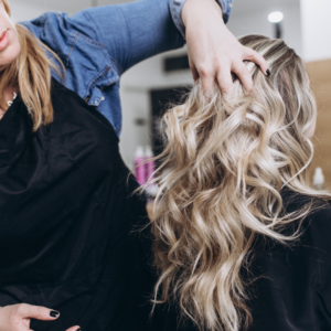 Hair stylist running hair through blonde, curly, long-haired client to add volume. 