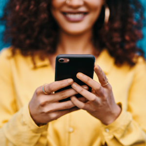 Smiling woman with curly hair holding a smart phone and looking at social media. 