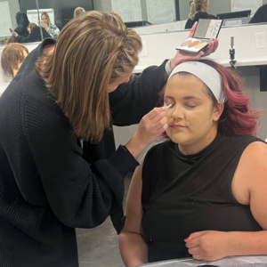 Cosmetology student enjoying a self-care makeup application from another student.