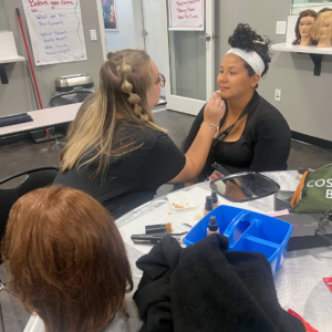 Cosmetology student enjoying a self-care makeup application from another student. 