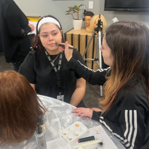 Cosmetology student enjoying a self-care makeup application from another student.