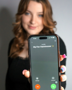 Cosmetology school student holding up phone that says "My Fav Hairdresser" is calling.
